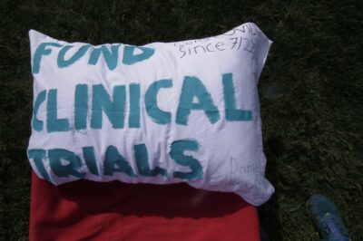 A pillow that reads "Fund clinical trials. Long COVID since 7/22. Daniel Lexuis"