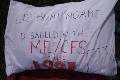 A pillow that reads "Liz Burlingame Disabled with ME/CFS since…" The year is cut off, but it's in the 1990's.