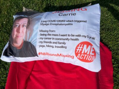 A pillow showing a picture of a smiling woman on the left. In the middle, it reads "Missing Carrie, Long COVID (2020) which triggered myalgic encephalomyelitis. Missing from: being the mom I want to be with my 5 year old, my career in community health, my friends and family, yoga, hiking, traveling. #MillionsMissing #MEAction